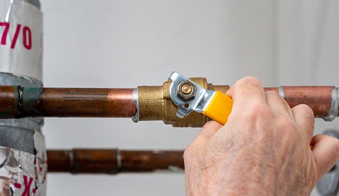 Hand turning off a water valve to stop supply